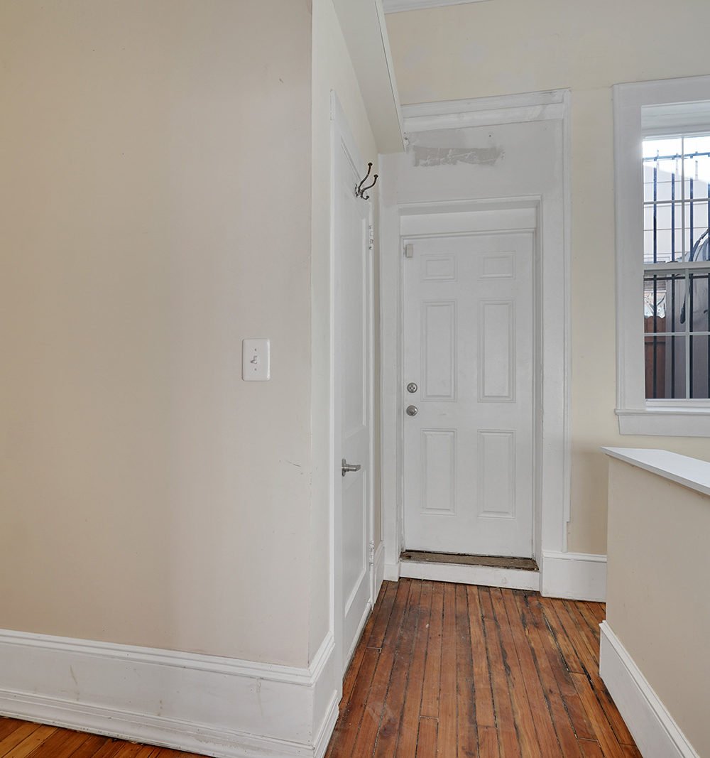 Entry hall with worn hardwood floors, a white paneled door, and a barred window.