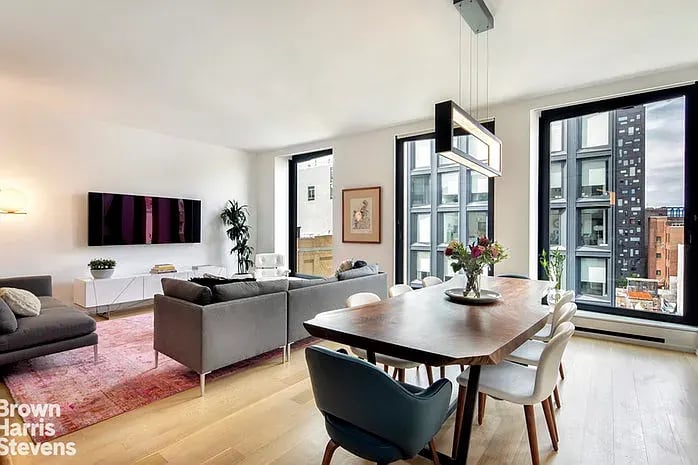 Open-plan living and dining room with floor-to-ceiling windows overlooking city buildings.
