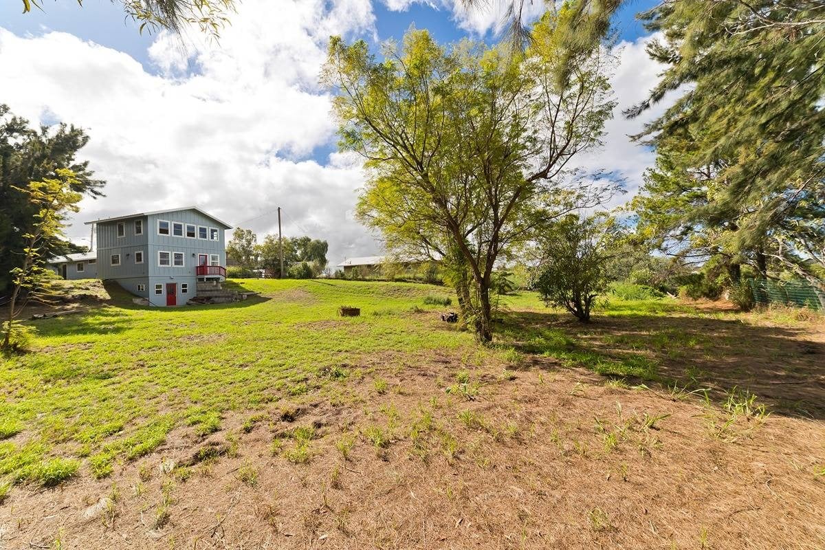 Blue-gray two-story home with a red balcony on a broad, tree-lined lot.