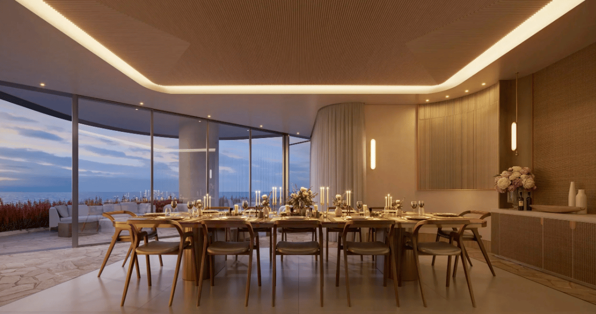 Furnished dining room with a long candlelit table and floor-to-ceiling windows overlooking the water.