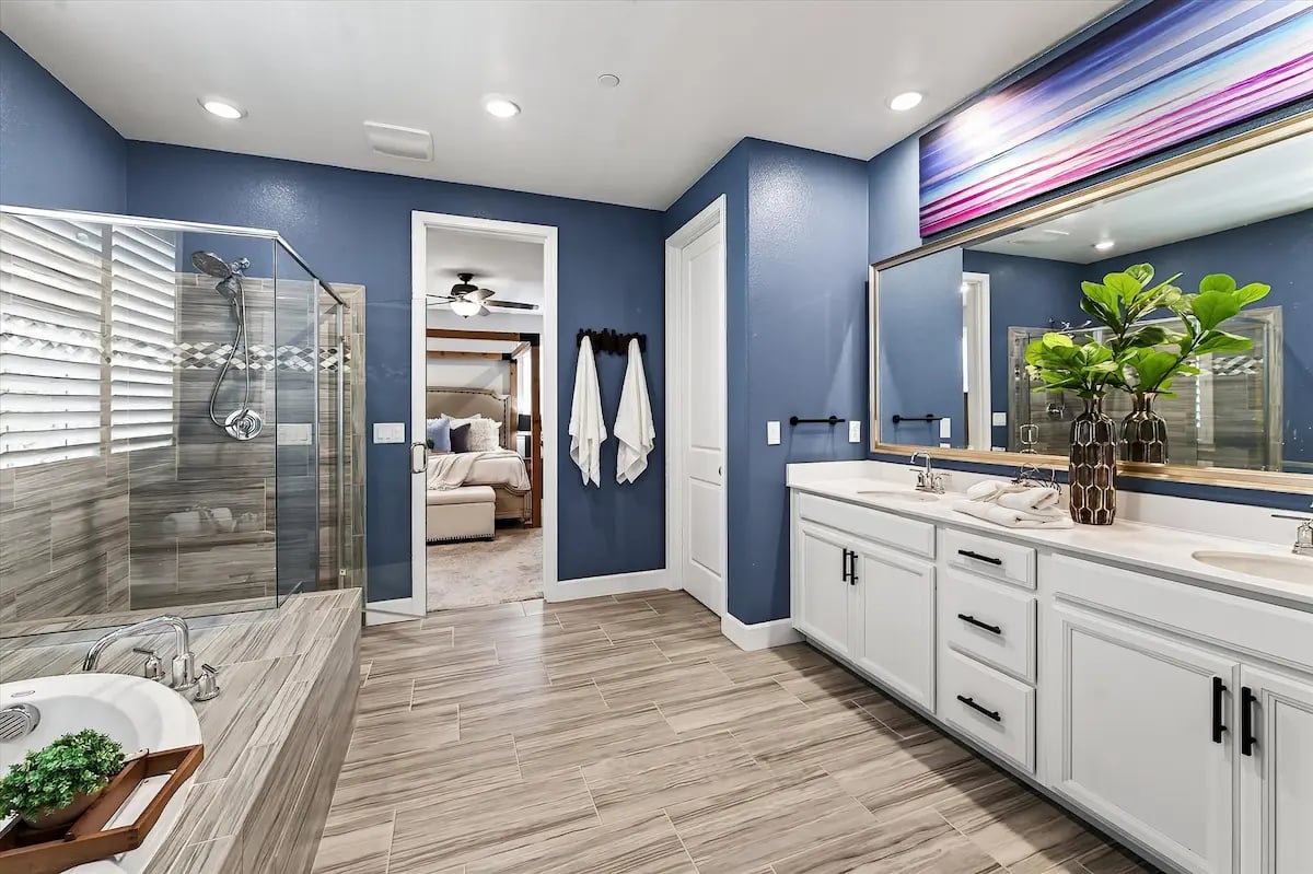 Bathroom with a glass shower, white double vanity, and blue walls.