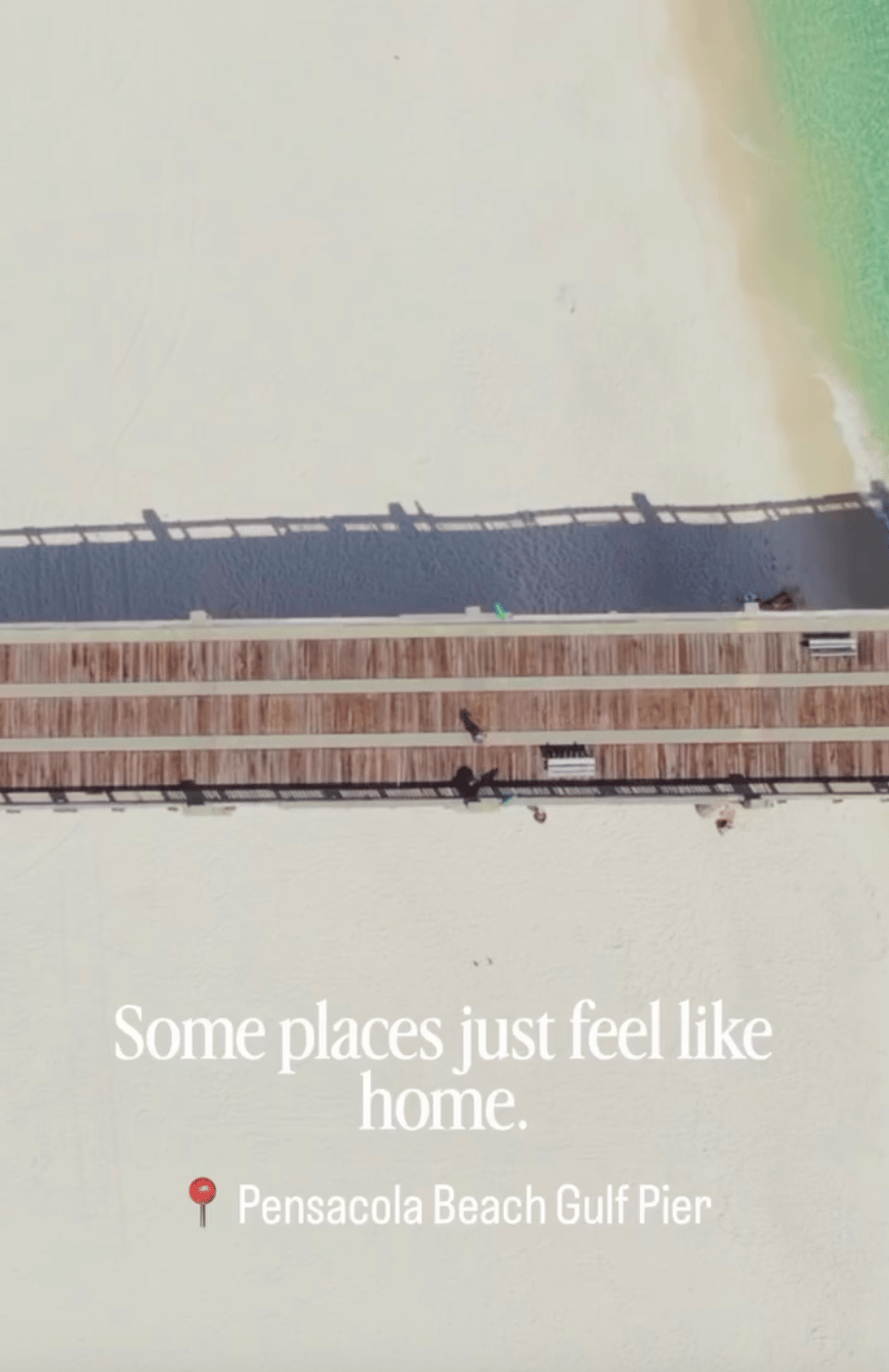 Pensacola Beach Gulf Pier stretches across pale sand beside turquoise water, seen from above.