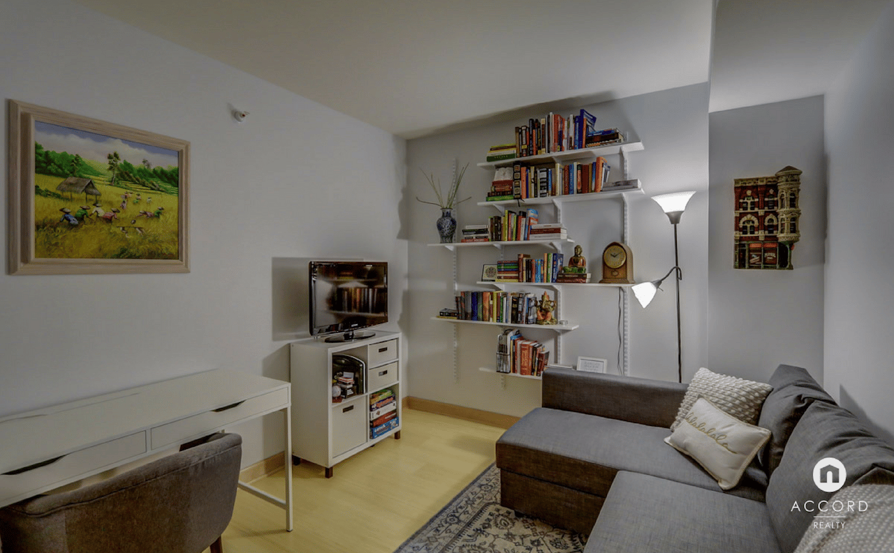 Condo living room with a gray sectional, book-filled shelves, and a white desk.