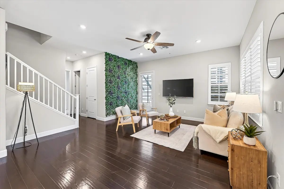 Living room with dark wood floors, a leafy accent wall, and cream seating.