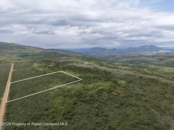 Aerial view of outlined undeveloped land beside a dirt road, with distant mountains.