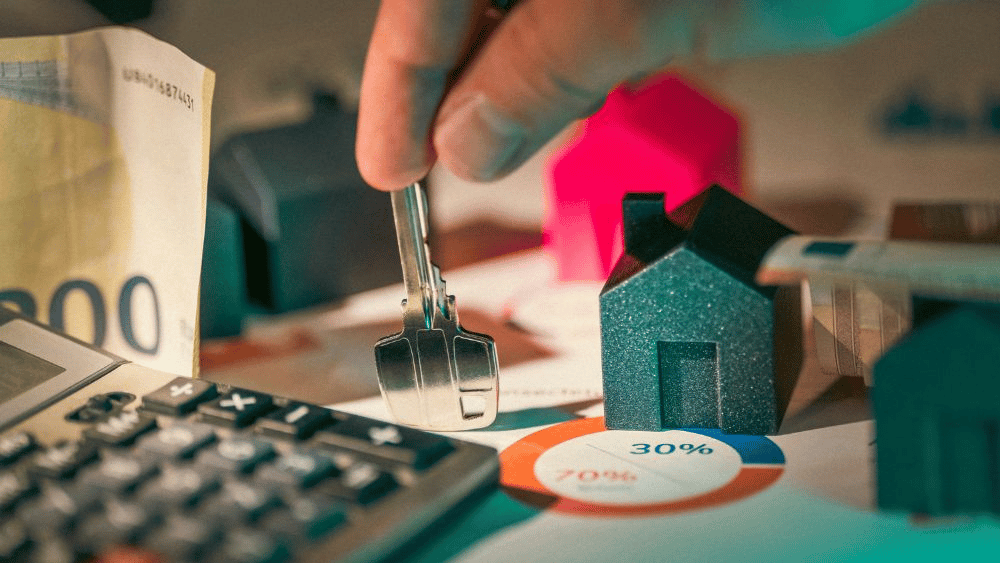 A hand holds a house key above miniature homes, a calculator, banknote, and 30/70 chart.