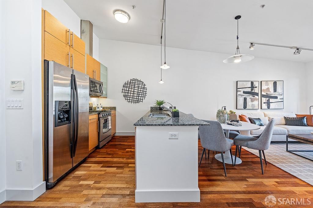 Open-plan kitchen with stainless steel appliances, a granite island, and an adjoining furnished living area.