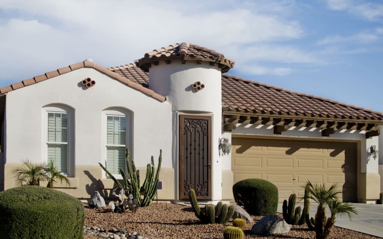 Mediterranean-style home with white stucco walls, terracotta roof, and desert landscaping.