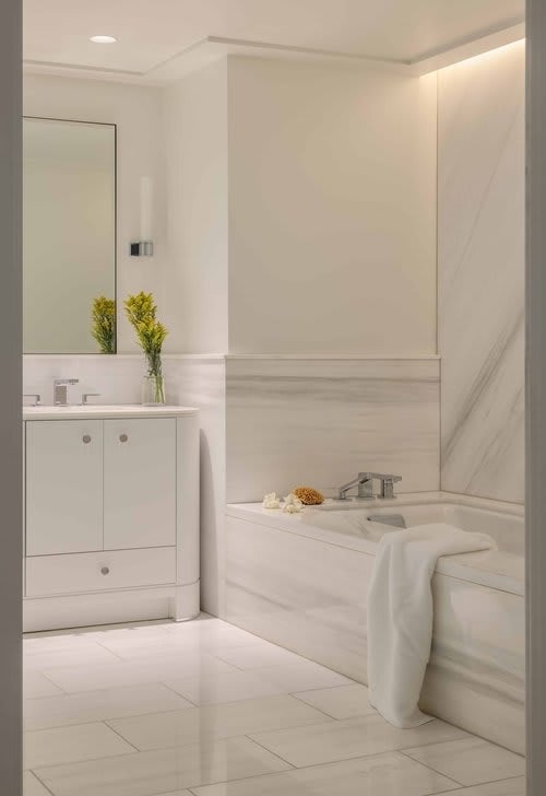 Marble bathroom with a white bathtub, matching vanity, and yellow flowers beside the sink.