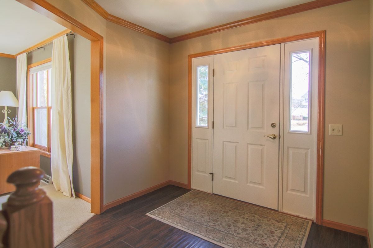 Entry foyer with a white front door, glass sidelights, hardwood floors, and warm wood trim.