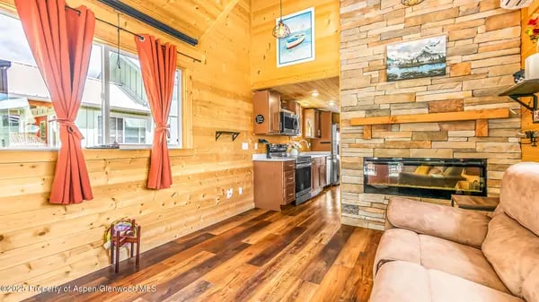 Open-plan living room with a stone fireplace, wood-paneled walls, and red curtains.