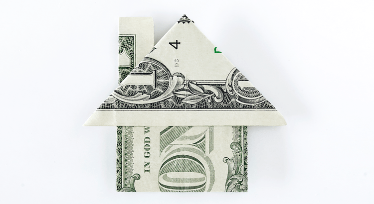 Origami house folded from a U.S. dollar bill against a white background. The bill is shaped with detailed roof and walls, symbolizing real estate investment.