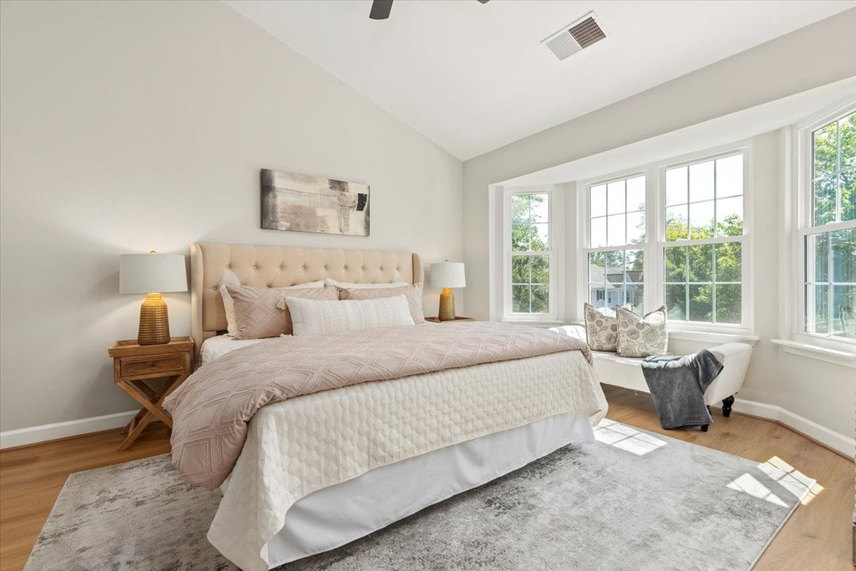 Bright bedroom with a tufted bed and a cushioned window seat beside tall windows.