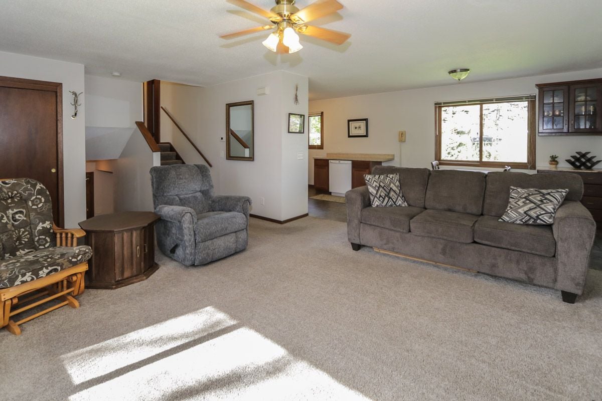 Living room with a gray sofa, recliner, wooden rocking chair, and sunlight across the carpet.