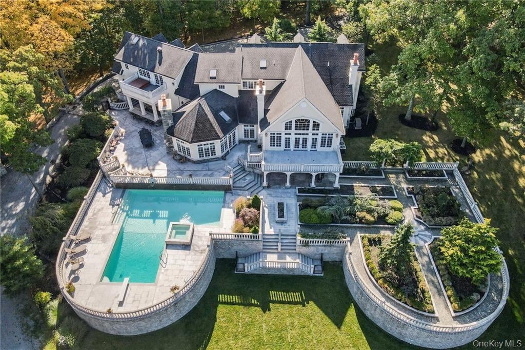 Large house with a swimming pool, curved stone terrace, and landscaped gardens, seen from above.