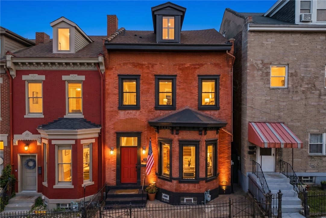 Brick row house at dusk with a red door, bay windows, and an American flag.