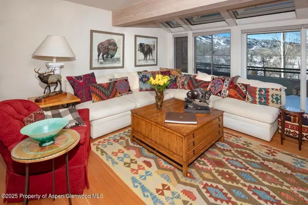 Living room with a white sectional, colorful pillows, and large windows overlooking a snowy mountain.