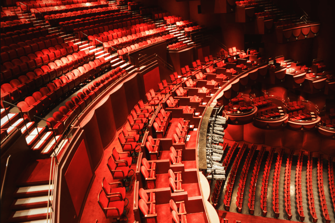 Empty theater auditorium with curved tiers of red seats and private boxes.