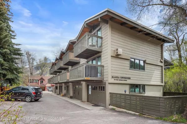 Townhouse building with multiple balconies, garage doors, and cars parked along the driveway.