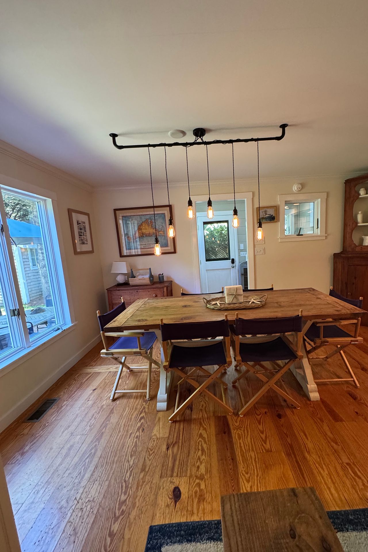 Dining room with a rustic wood table, canvas chairs, hardwood floors, and hanging pendant lights.