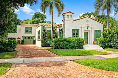 Stucco home with terracotta tile roofs, a brick driveway, and tropical landscaping.