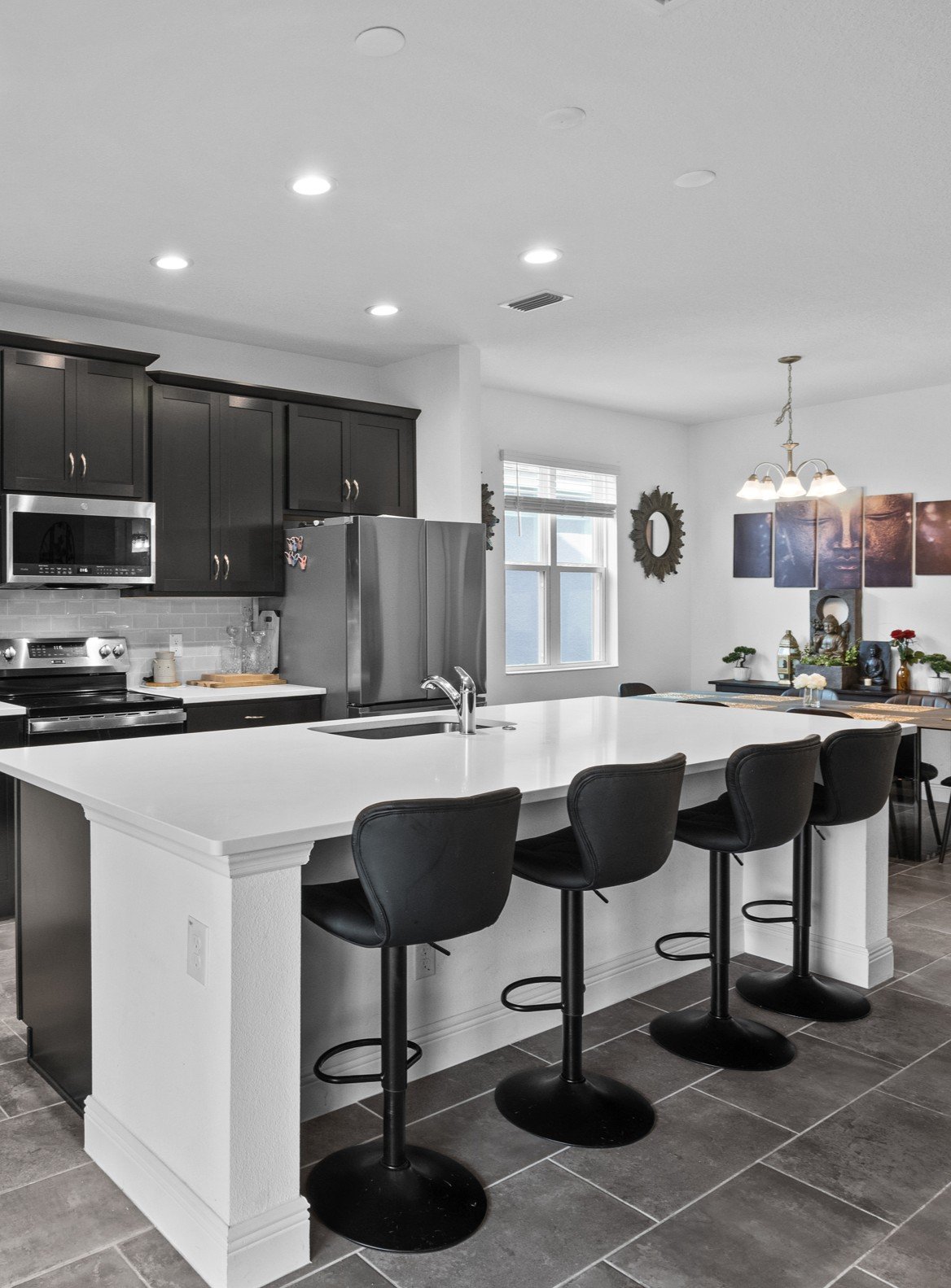 Kitchen with dark cabinets, stainless appliances, and a large white island lined with black bar stools.