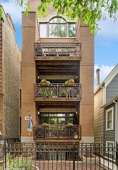 Brown brick residence with three balconies and a fenced courtyard.