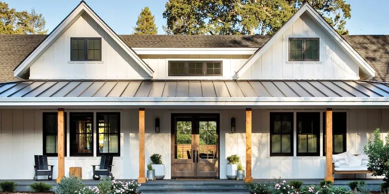 White modern farmhouse with twin front gables, a metal porch roof, and a furnished covered porch.