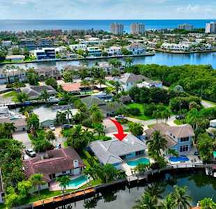 Aerial view of canal-front homes, with a red arrow pointing to a gray-roofed house and pool.