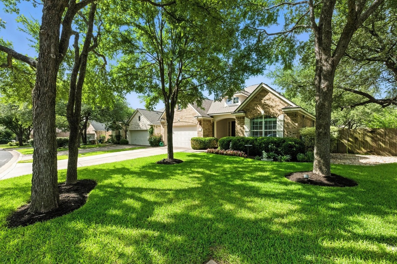 Brick home with an attached garage, framed by mature trees and a broad green lawn.