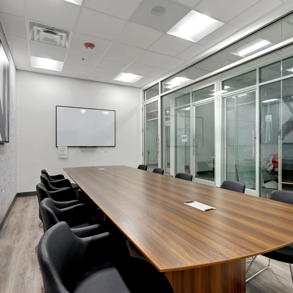 Conference room with a long wood-grain table, black chairs, and glass walls.