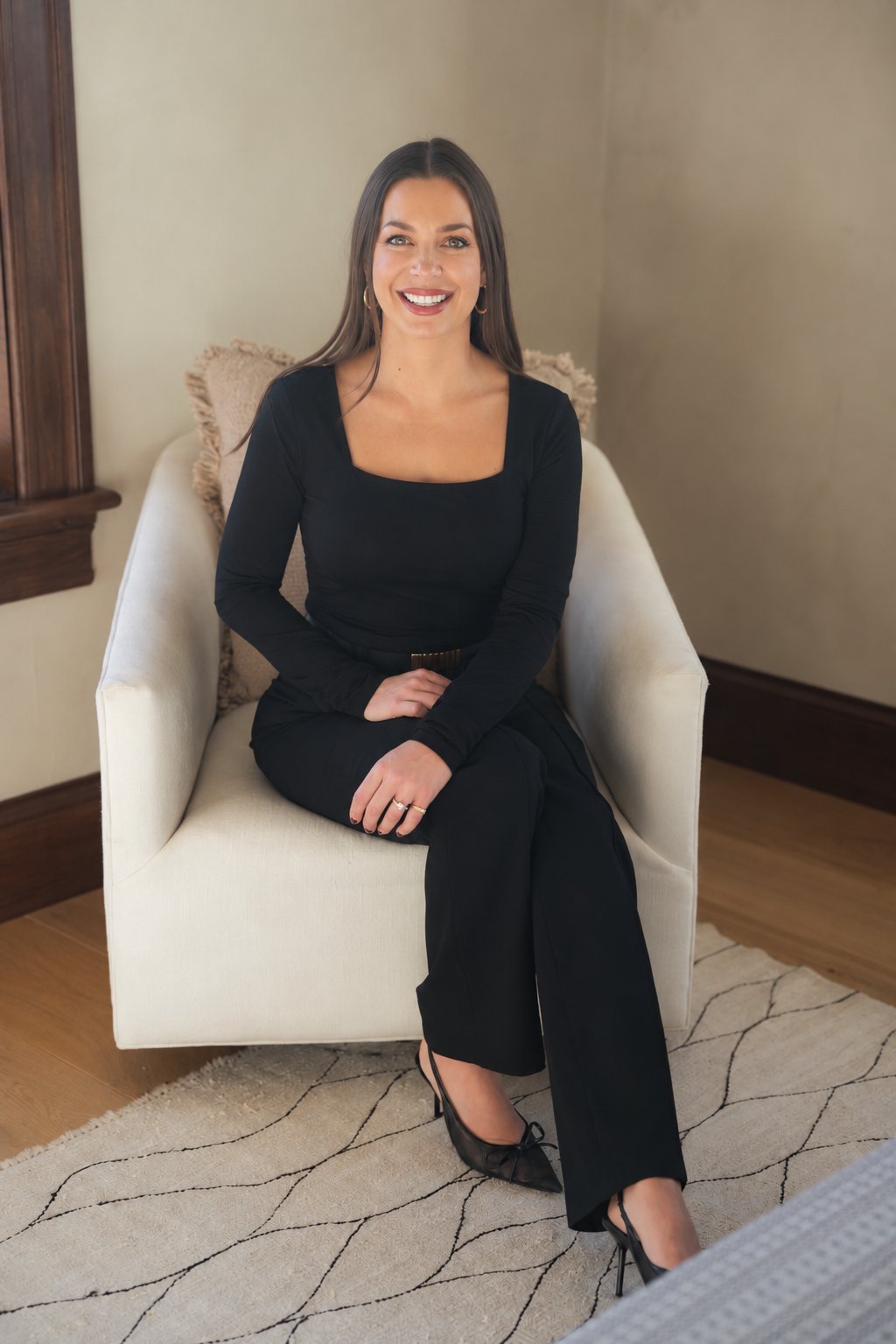 Rachael McMasters seated in a white armchair, wearing a black outfit.