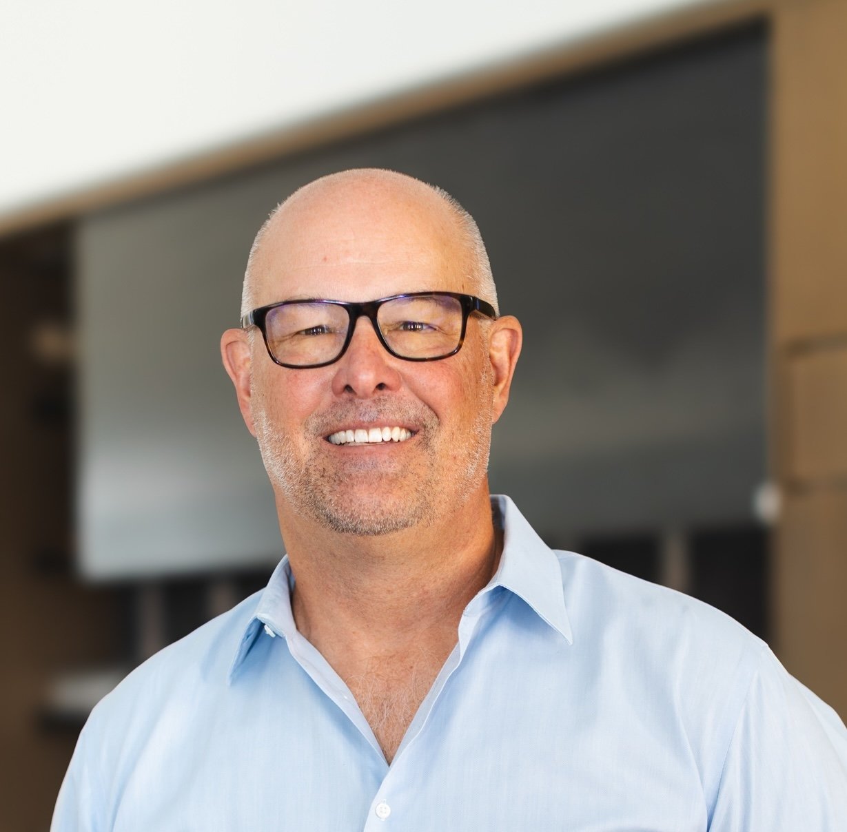 Daniel Zemke smiling in black glasses and a light blue shirt.