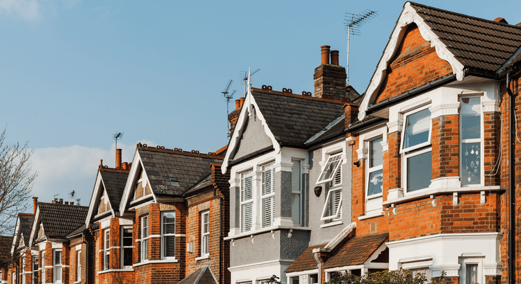 A row of traditional British terraced houses with red brick exteriors and white window frames.