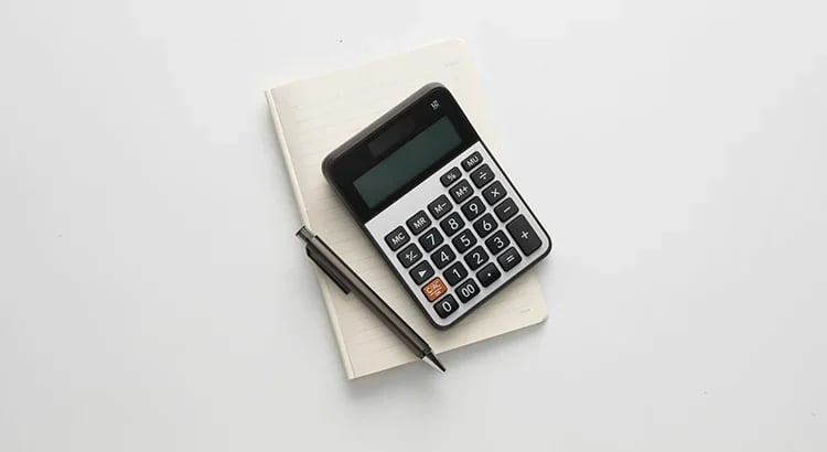 A close-up of a calculator and a pen placed on top of a white notebook. This appears to be a simple and clean setup, likely related to financial or educational content.