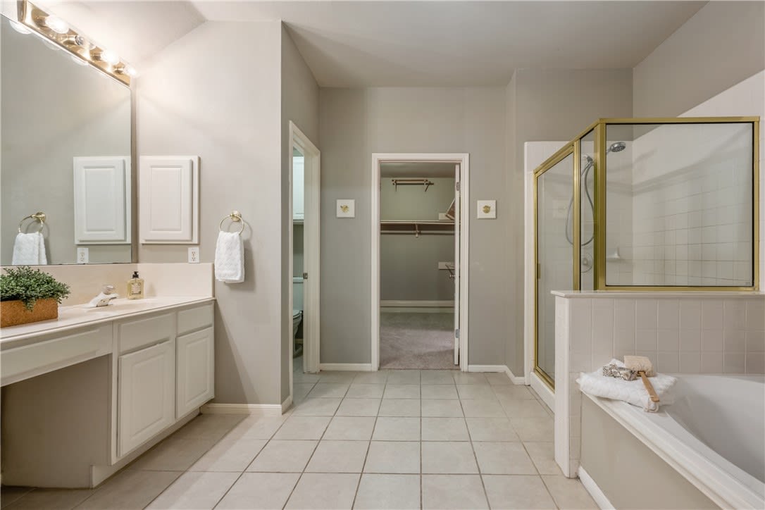 Bathroom with a long white vanity and a bathtub beside a gold-framed glass shower.