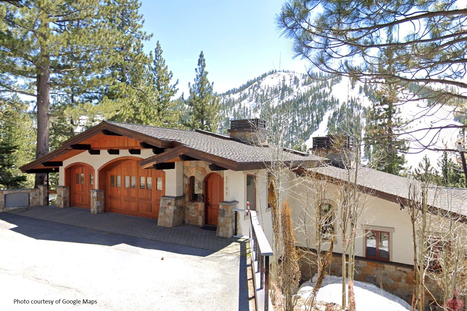 Mountain home with wooden garage doors and stone accents, backed by a snowy, pine-covered peak.
