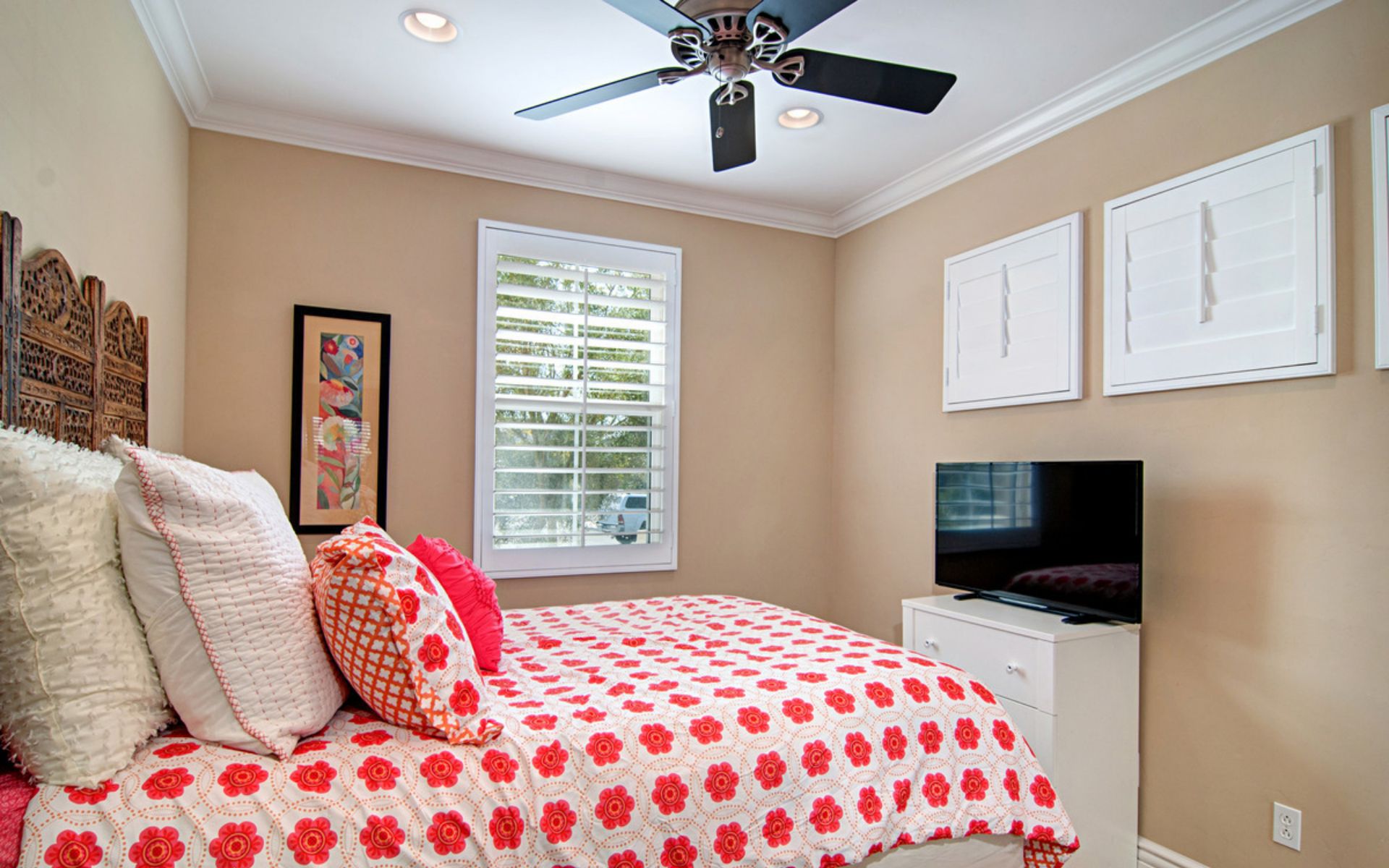 Bedroom with red floral bedding, plantation shutters, and a ceiling fan.