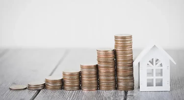 A stack of coins next to a small house model, symbolizing financial savings for a home or real estate investment.