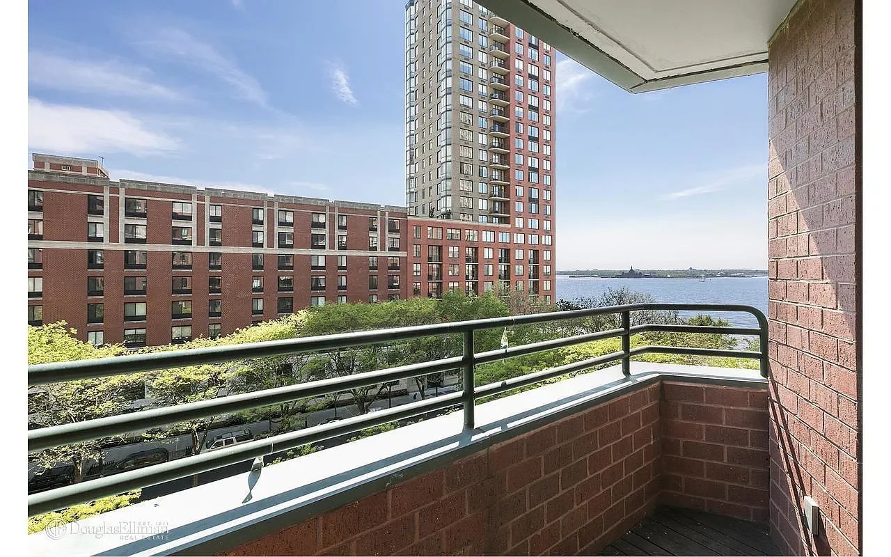 Brick balcony overlooking neighboring buildings and water, with a black metal railing.