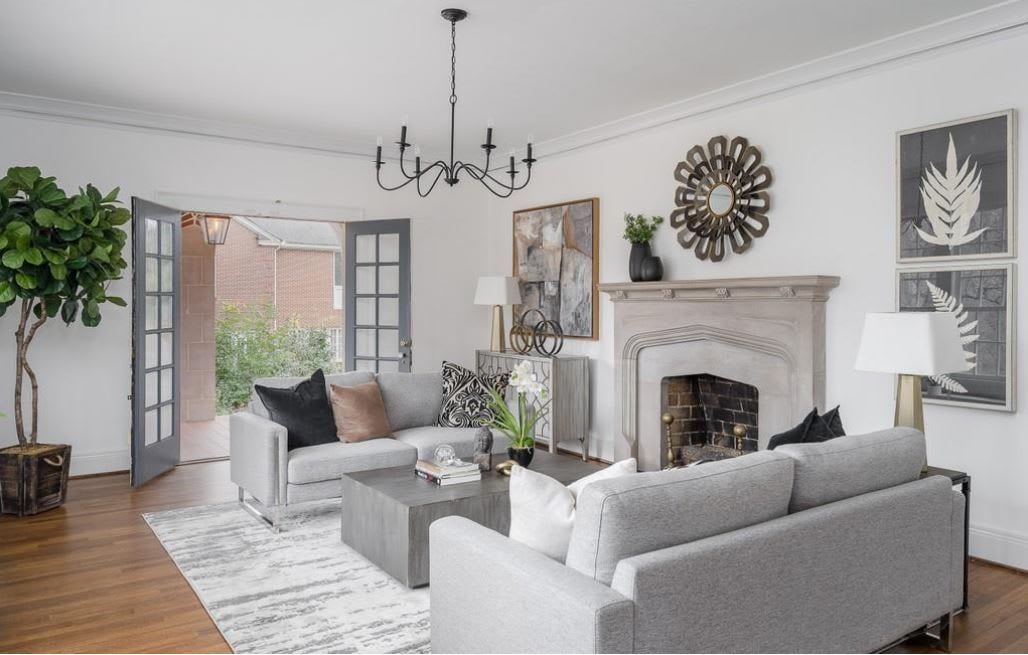 A cozy living room with a mirror above the fireplace, a couch, a wooden coffee table, light beige walls, and hardwood floors.