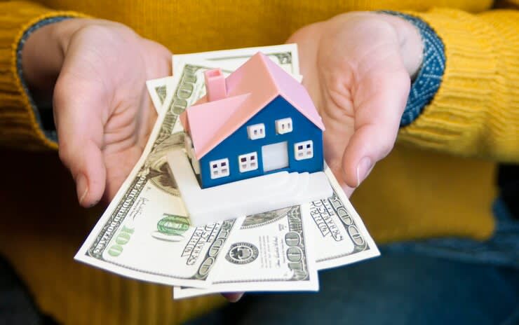 model house on top of paper bills in womans hands