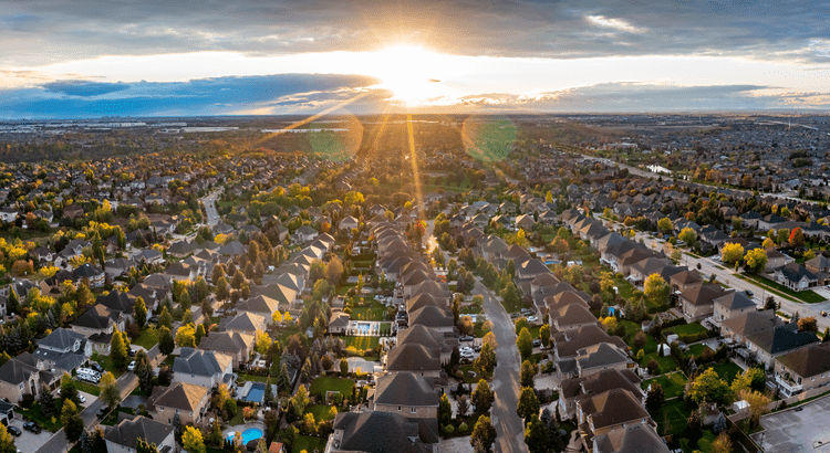 Aerial view of a residential neighborhood bathed in warm hues of sunset, showcasing rooftops and tree-lined streets.