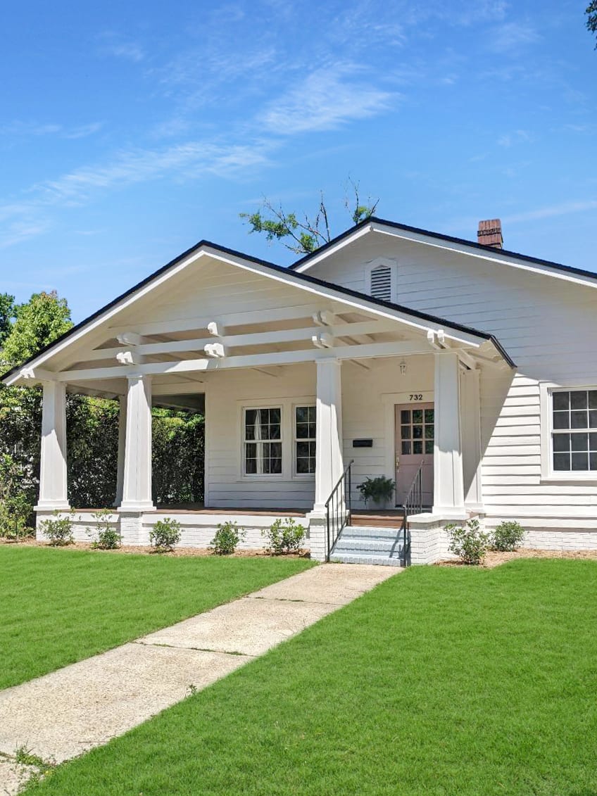 A front view of a white single-story house with a manicured lawn and a pathway leading to the porch.