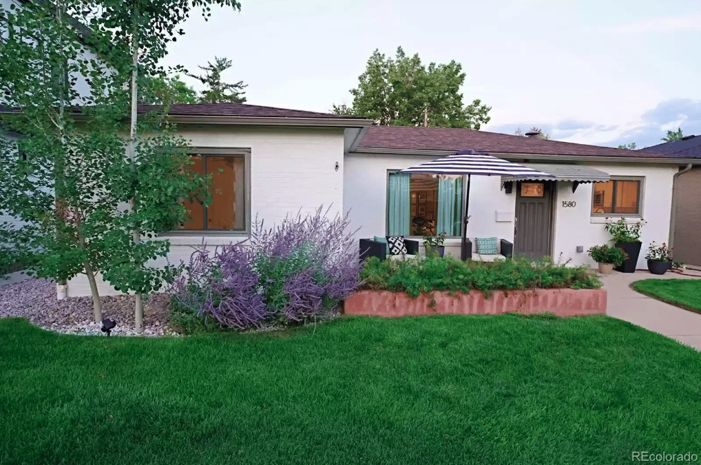 Single-story white house with a striped patio umbrella and landscaped front yard.