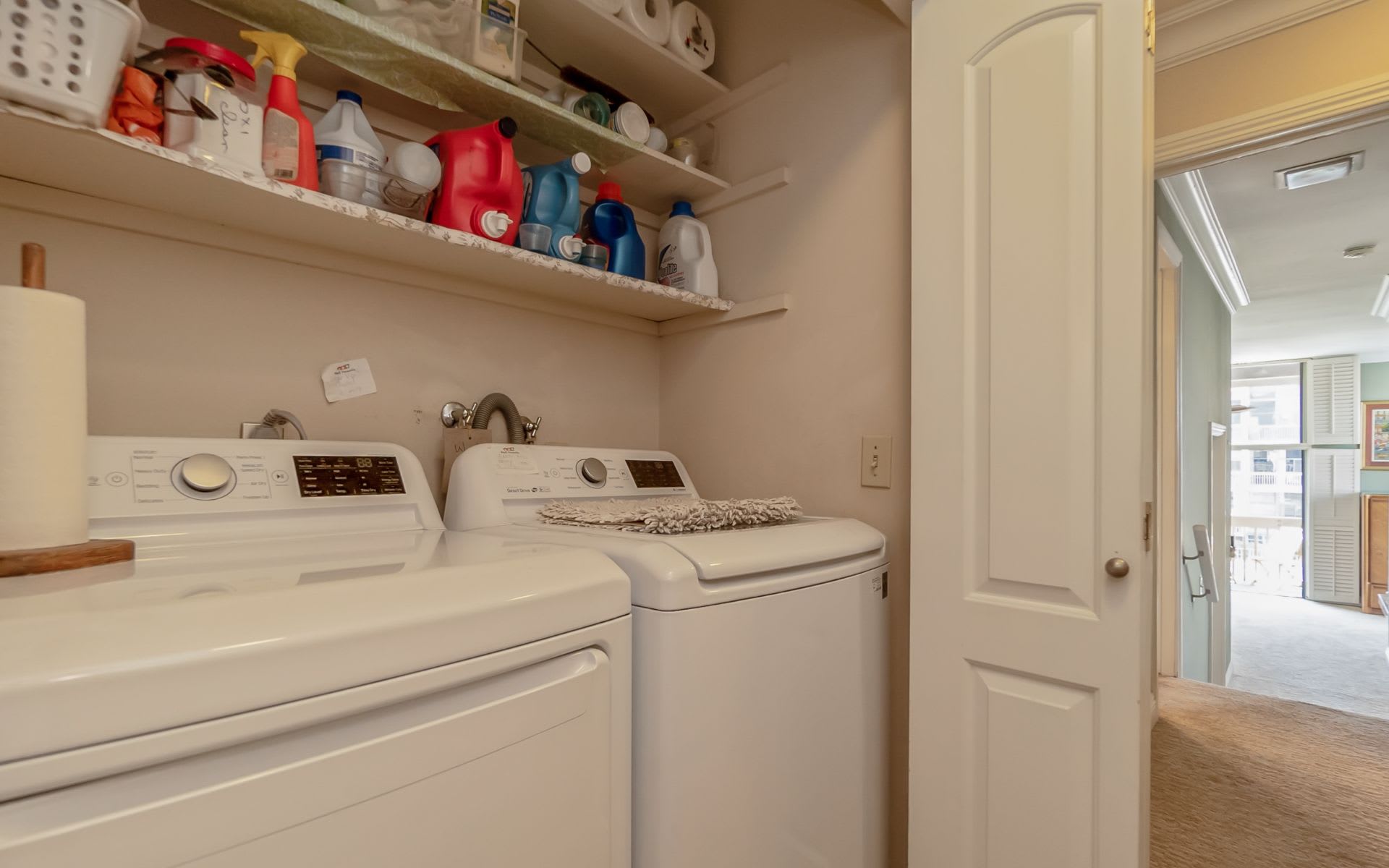 Laundry room with white washer and dryer beneath shelves of laundry supplies.