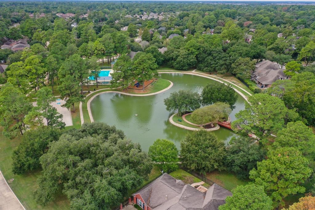 Aerial view of a wooded neighborhood pond with walking paths and a swimming pool.