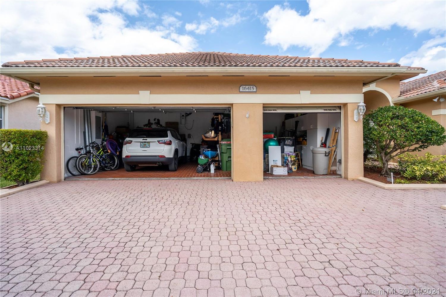 Home with two open garage bays, a car and bicycles inside, and a wide paver driveway.