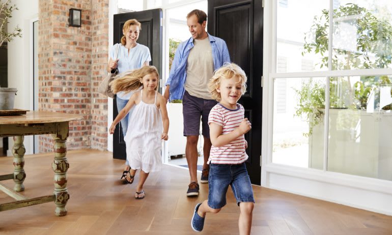 Bright home interior with hardwood floors and brick wall as a family walks in.