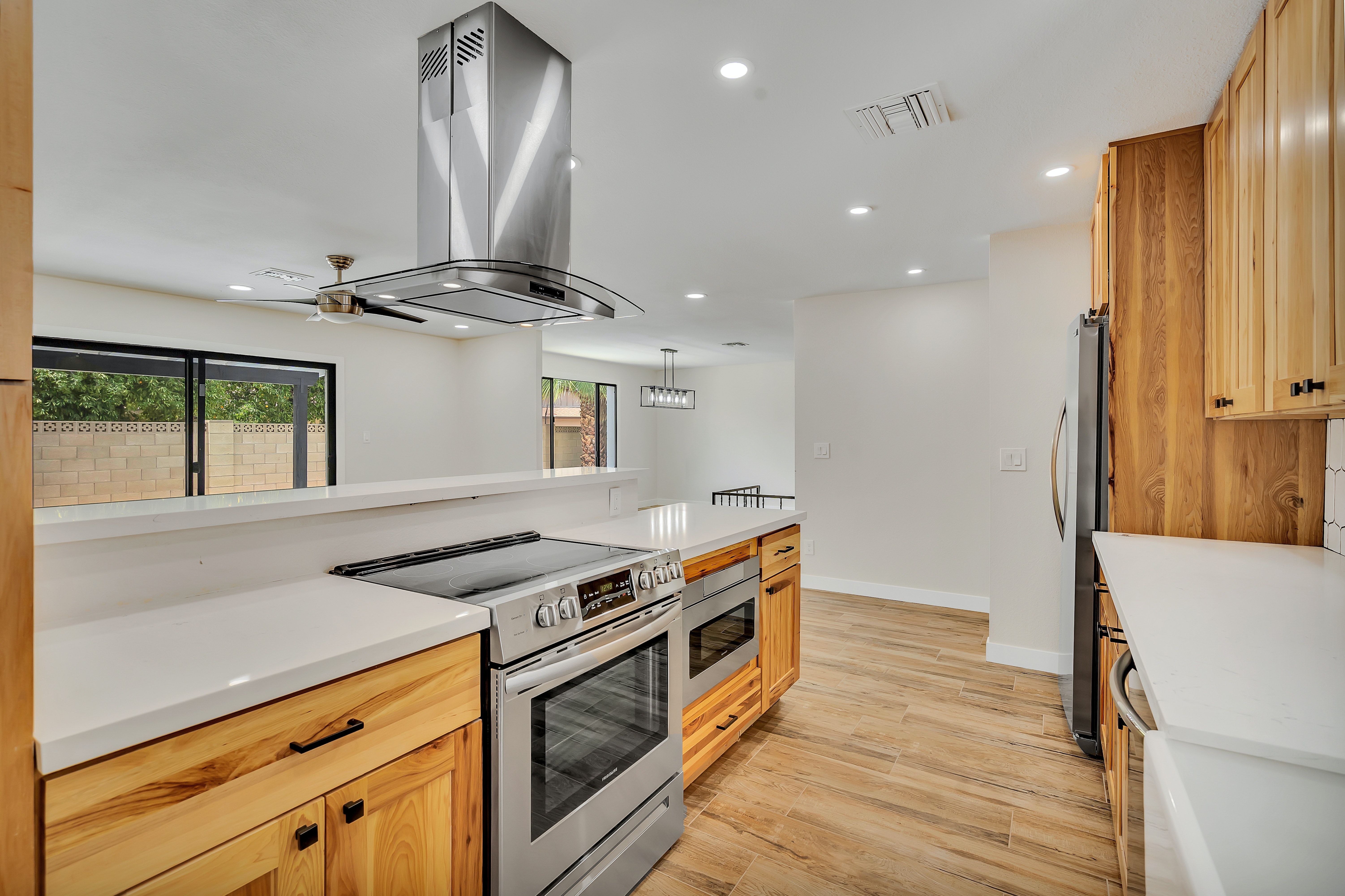 Modern kitchen with honey-toned wood cabinets, white counters, and a prominent stainless steel range hood.